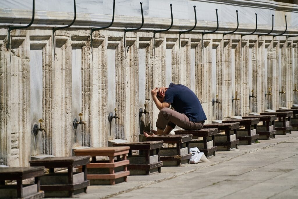 A person performing wudu (ablution) at outdoor taps / fountains